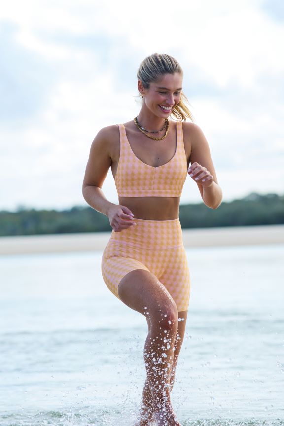 Model in the water at the beach wearing a pink watercolour check print Reversible Swim Sports Bra and matching Reversible Swim Phone Pocket Bike Short